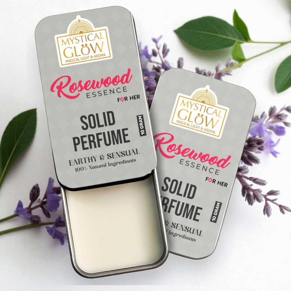 Alcohol Free, Rosewood Essence Solid Perfume for Women in a round tin surrounded by rose petals, rosewood slices, and amber stone on a white background.