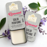 Alcohol Free perfume for women, Rosewood Essence Solid Perfume for Women in a round tin surrounded by rose petals, rosewood slices, and amber stone on a white background.